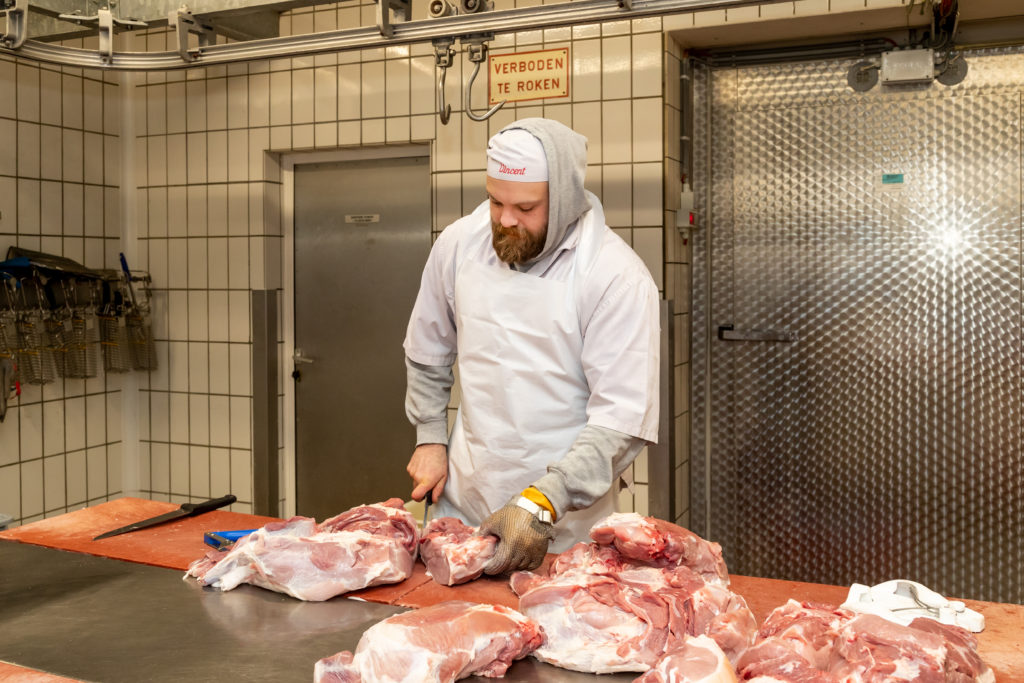 Slager die vlees in stukken snijdt bij Slagere Vincent. 
