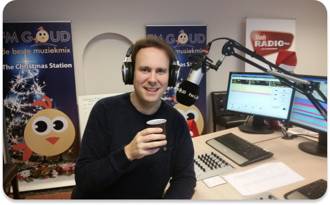 De radiopresentator van radiozender FM-goud die in zijn studio achter de microfoon zit.